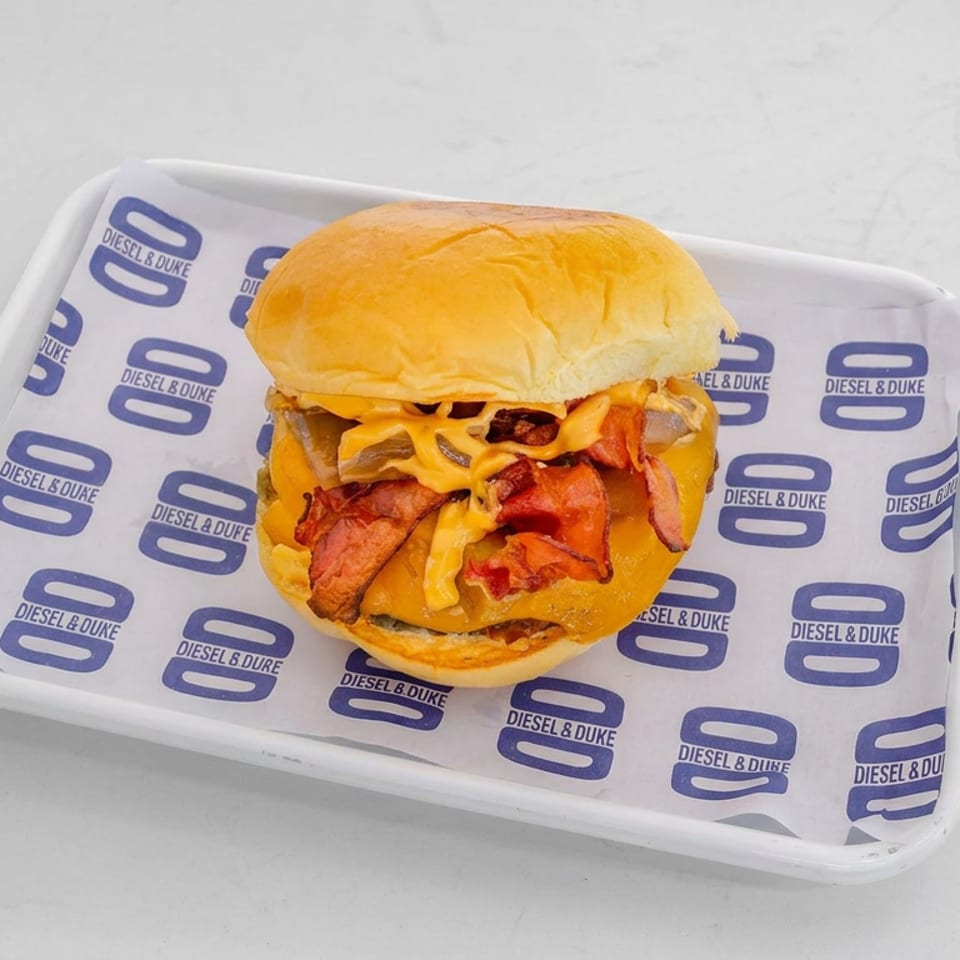 Bacon cheeseburger with melted cheese and grilled onions served on a branded Diesel & Duke tray.